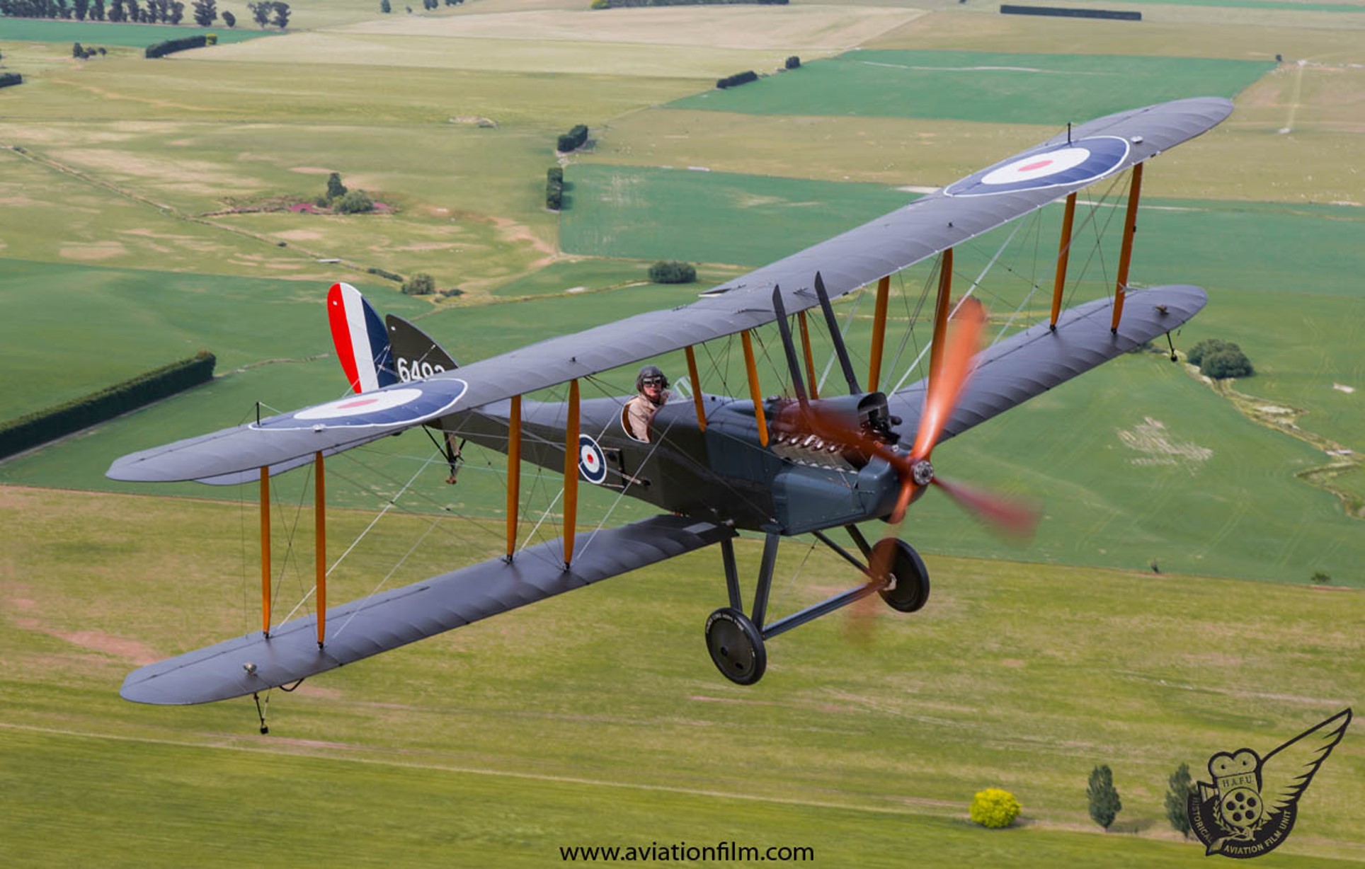 A BE12 biplane in flight over patchwork fields, RAF roundels on the upper wing.